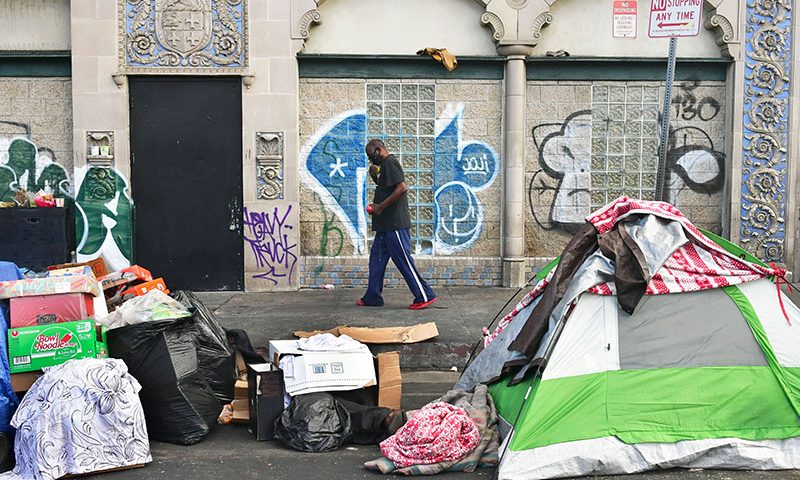 A man walks past tents housing the homeless on the streets in the Skid Row community of Los Angeles, California on April 26, 2021. - A federal judge overseeing a lawsuit that seeks to end the city's Skid Row homelessness crisis isn't backing down from his order requiring that all indigent persons in the area be offered shelter within six months. US District Judge David O. Carter is opening the door for more discussions by setting additional hearing dates and clarifying some portions of his ruling. (Photo by Frederic J. BROWN / AFP) (Photo by FREDERIC J. BROWN/AFP via Getty Images)