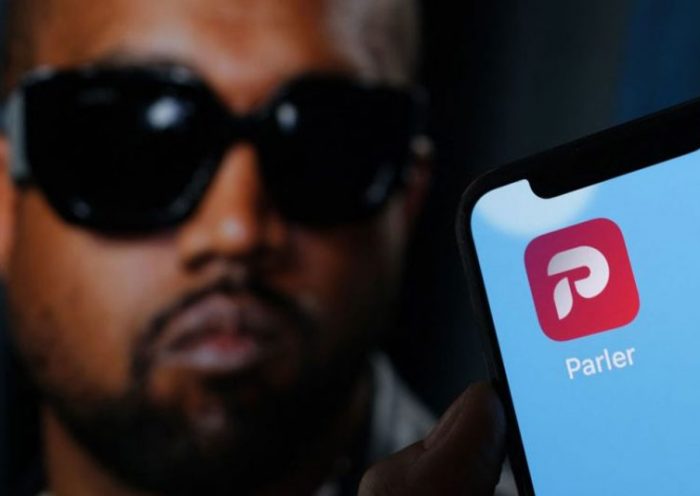 This illustration photo shows the Parler social network app logo on a cell phone screen with a picture of US rapper Kanye West in the background in Los Angeles, October 17, 2022. - Social network Parler announced on October 17 a deal for Kanye West to buy the platform popular with US conservatives, just over a week after the rapper's Twitter and Instagram accounts were restricted over anti-Semitic posts. West -- now known as Ye -- has recently alienated fans and business partners with anti-Semitic comments, interest in racist conspiracy theories and wearing a provocative "White Lives Matter" T-shirt at Paris fashion week. (Photo by Chris DELMAS / AFP) (Photo by CHRIS DELMAS/AFP via Getty Images)