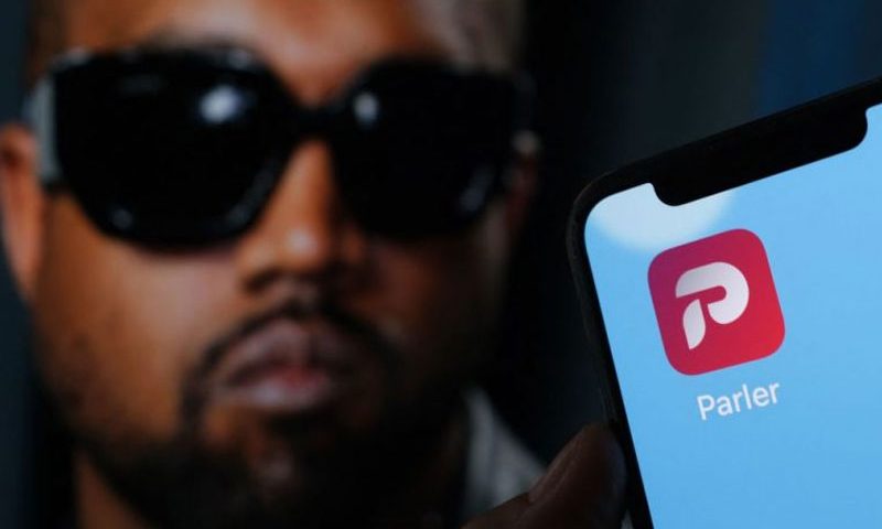 This illustration photo shows the Parler social network app logo on a cell phone screen with a picture of US rapper Kanye West in the background in Los Angeles, October 17, 2022. - Social network Parler announced on October 17 a deal for Kanye West to buy the platform popular with US conservatives, just over a week after the rapper's Twitter and Instagram accounts were restricted over anti-Semitic posts. West -- now known as Ye -- has recently alienated fans and business partners with anti-Semitic comments, interest in racist conspiracy theories and wearing a provocative "White Lives Matter" T-shirt at Paris fashion week. (Photo by Chris DELMAS / AFP) (Photo by CHRIS DELMAS/AFP via Getty Images)