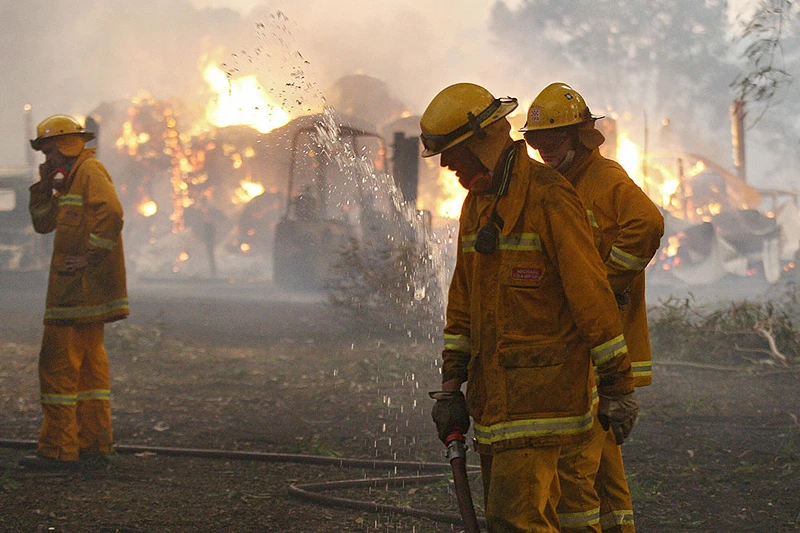 Country Fire Authority (CFA) volunteers pack away their hose as a barn burns in the background after they managed to save the house close to Labertouche, some 125 kilometres west of Melbourne, on February 7, 2009. More than 40 blazes raged across two states as a once-in-a-century heatwave pushed the mercury as high as 46 degrees Celsius (115 Fahrenheit) with fire bans in place across much of the south-east, with conditions said to be the worst since the Ash Wednesday wildfires of 1983, which killed 75 people and razed 2,500 homes. AFP PHOTO/William WEST (Photo credit should read WILLIAM WEST/AFP via Getty Images)