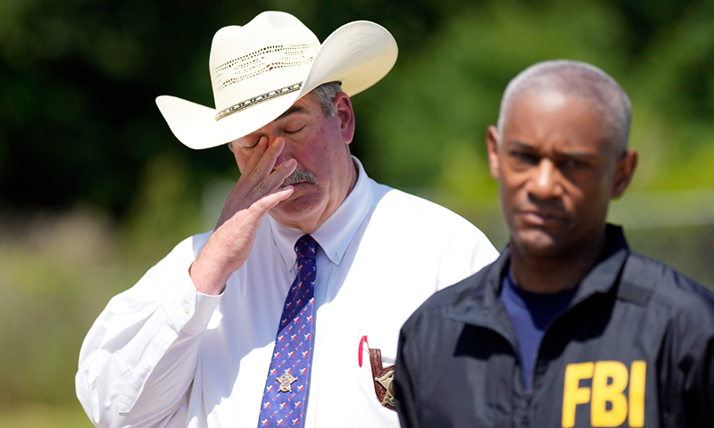 San Jacinto County Sheriff Greg Capers, left, wipes his eye as FBI Houston Special Agent in Charge James Smith speaks during a news conference, Sunday, April 30, 2023, in Cleveland, Texas. The search for a Texas man who allegedly shot his neighbors after they asked him to stop firing off rounds in his yard stretched into a second day Sunday, with authorities saying the man could be anywhere by now. The suspect fled after the shooting Friday night that left five people dead, including a young boy. (AP Photo/David J. Phillip)