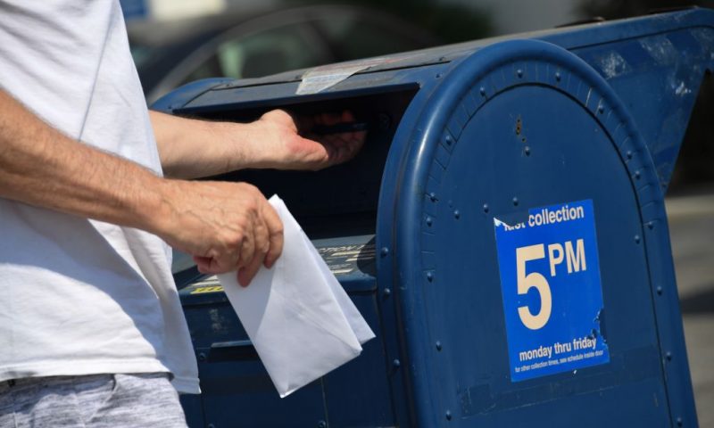 A person mails a letter at a mailbox outside a post office in Los Angeles, California, August 17, 2020. - The United States Postal Service is popularly known for delivering mail despite snow, rain or heat, but it faces a new foe in President Donald Trump. Ahead of the November 3 elections in which millions of voters are expected to cast ballots by mail due to the coronavirus, Trump has leveled an unprecedented attack at the USPS, opposing efforts to give the cash-strapped agency more money as part of a big new virus-related stimulus package, even as changes there have caused delays in mail delivery. (Photo by Robyn Beck / AFP) (Photo by ROBYN BECK/AFP via Getty Images)