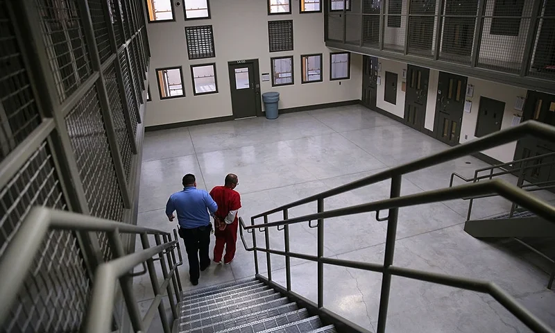 ADELANTO, CA - NOVEMBER 15: A guard escorts an immigrant detainee from his 'segregation cell' back into the general population at the Adelanto Detention Facility on November 15, 2013 in Adelanto, California. Most detainees in segregation cells are sent there for fighting with other immigrants, according to guards. The facility, the largest and newest Immigration and Customs Enforcement (ICE), detention center in California, houses an average of 1,100 immigrants in custody pending a decision in their immigration cases or awaiting deportation. The average stay for a detainee is 29 days. The facility is managed by the private GEO Group. ICE detains an average of 33,000 undocumented immigrants in more than 400 facilities nationwide. (Photo by John Moore/Getty Images)