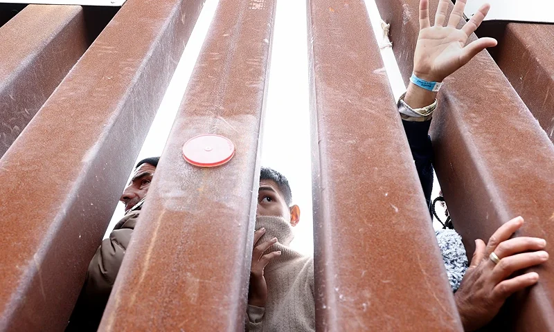 SAN DIEGO, CALIFORNIA - MAY 13: Immigrants seeking asylum in the U.S., who are stuck in a makeshift camp between border walls between the U.S. and Mexico, reach and look through the border wall as volunteers offer assistance on the other side on May 13, 2023 in San Diego, California. Some of the hundreds of migrants at the open air camp have been waiting for days in limbo for a chance to plead for asylum as local volunteer groups are providing food and other necessities. The U.S. government's Covid-era Title 42 policy, which for the past three years had allowed for the quick expulsion of irregular migrants entering the country, expired on the evening on May 11th. (Photo by Mario Tama/Getty Images)