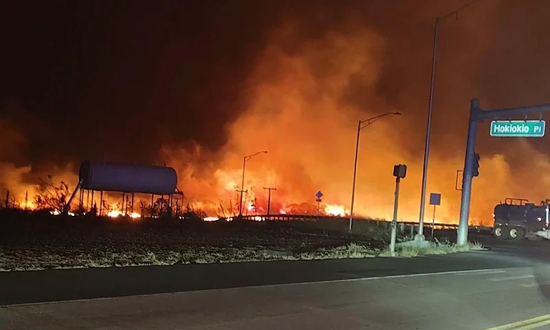 This photo provided by County of Maui shows fire and smoke filling the sky from wildfires on the intersection at Hokiokio Place and Lahaina Bypass in Maui, Hawaii on Tuesday, Aug. 8, 2023. Wildfires in Hawaii fanned by strong winds burned multiple structures in areas including historic Lahaina town, forcing evacuations and closing schools in several communities Wednesday, and rescuers pulled a dozen people escaping smoke and flames from the ocean. (Zeke Kalua/County of Maui via AP)