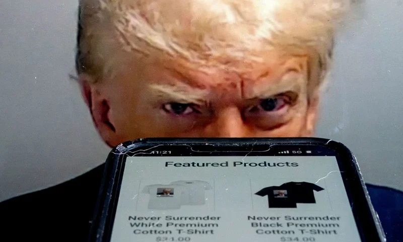 (ILLUSTRATION) This photo illustration created in Washington, DC, on August 27, 2023, shows the mugshot of former US President Donald Trump next to a website called Trump Save America JFC, a joint fundraising committee on behalf of Donald J. Trump for President 2024, which is selling merchandise bearing his mugshot. For most people, a police mug shot would be a badge of dishonor they would do anything to erase. For Donald Trump, it's a branding opportunity and political weapon. The scowling, vengeful stare captured at a Georgia jail on August 24, 2023, after Trump was booked on racketeering and conspiracy charges has quickly become his 2024 campaign symbol. T-shirts, mugs, stickers and beverage coolers bearing the first mug shot of a serving or former US president were put out by his team within hours of the photo's release. (Photo by Stefani Reynolds / AFP) (Photo by STEFANI REYNOLDS/AFP via Getty Images)