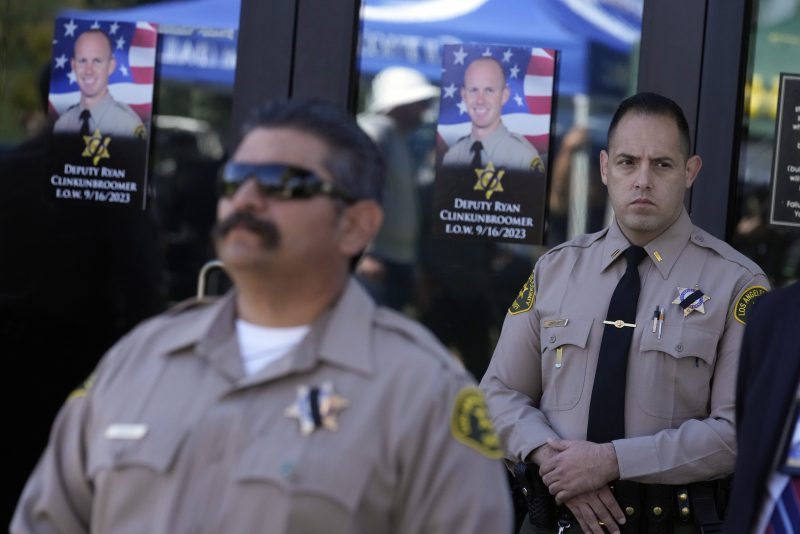 Photos of Los Angeles County sheriffs deputy Ryan Clinkunbroomer are placed at the entrance of the Palmdale Sheriff's Station during a press to announce an arrest in the ambush killing of Clinkunbroomer Monday, Sept. 18, 2023, in Palmdale, Calif. Clinkunbroomer was shot and killed while sitting in his patrol car Saturday evening in Palmdale. (AP Photo/Marcio Jose Sanchez)