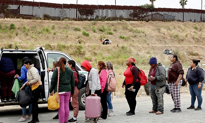 SAN DIEGO, CALIFORNIA - MAY 13: A U.S. Border Patrol agent keeps watch as immigrants enter a vehicle to be transported from a makeshift camp between border walls, between the U.S. and Mexico, on May 13, 2023 in San Diego, California. Some of the immigrants at the open air camp have been waiting for days in limbo for a chance to plead for asylum while local volunteer groups are providing food and other necessities. The U.S. government's Covid-era Title 42 policy, which for the past three years had allowed for the quick expulsion of irregular migrants entering the country, expired on the evening of May 11. (Photo by Mario Tama/Getty Images)