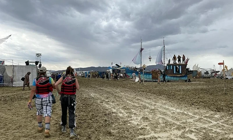 TOPSHOT - Attendees walk through a muddy desert plain on September 2, 2023, after heavy rains turned the annual Burning Man festival site in Nevada's Black Rock desert into a mud pit. Tens of thousands of drenched festivalgoers were stranded on September 3, 2023, in deep, sticky mud in the Nevada desert after torrential rain turned the annual Burning Man gathering into a quagmire. All events at the counterculture festival, which drew some 70,000 people, were canceled after rain tore down structures for dance parties, art installations and other eclectic entertainment. (Photo by Julie JAMMOT / AFP) (Photo by JULIE JAMMOT/AFP via Getty Images)