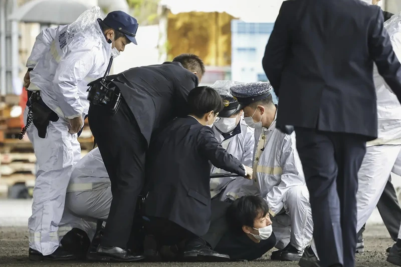 A man believed to be a suspect, center on the ground, is caught by police after he allegedly threw “the suspicious object,” as Japanese Prime Minister Fumio Kishida visited Saikazaki port for an election campaign event in Wakayama, western Japan Saturday, April 15, 2023. Kishida was evacuated unharmed Saturday after someone threw an explosive device in his direction while he was campaigning at the fishing port in western Japan, officials said.(Kyodo News via AP)
