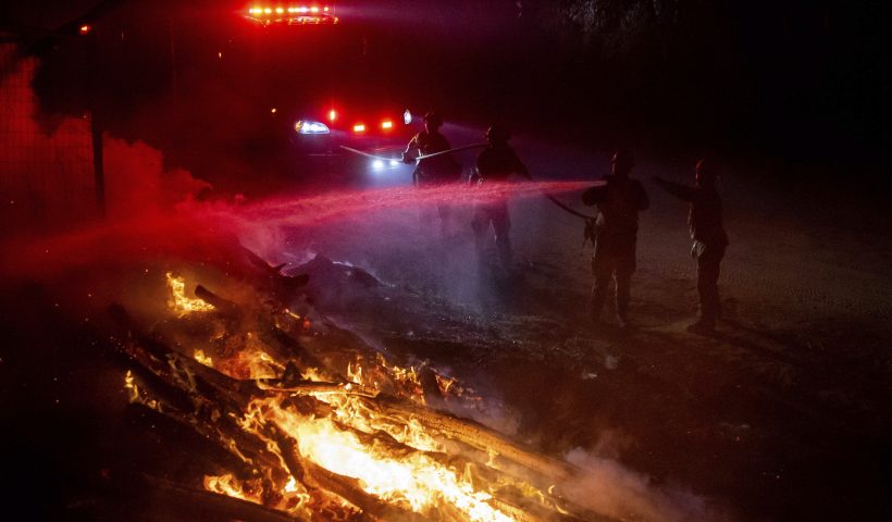 Firefighters douse flames while battling a wildfire called the Highland Fire in Aguanga, Calif., Monday, Oct. 30, 2023. A wildfire fueled by gusty Santa Ana winds ripped through rural land southeast of Los Angeles on Monday, forcing thousands of people from their homes, fire authorities said. (AP Photo/Ethan Swope)