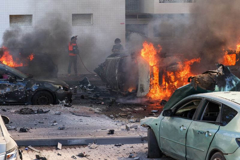 TOPSHOT - People try to extinguish fire on cars following a rocket attack from the Gaza Strip in Ashkelon, southern Israel, on October 7, 2023. Palestinian militant group Hamas has launched a "war" against Israel, Defence Minister Yoav Gallant said, after barrages of rockets were fired from the Gaza Strip into Israeli territory on October 7. (Photo by AHMAD GHARABLI / AFP) (Photo by AHMAD GHARABLI/AFP via Getty Images)