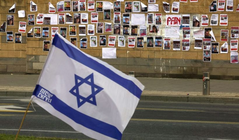 The Israeli flag is place close to a wall plastered with images of Israeli hostages snatched by the Palestinian militant group Hamas last week in a surprise attack into Israel, outside the Ministry of Defense in Tel Aviv on October 16, 2023. The Israeli military on October 16, raised the figure to 199 people confirmed to have been abduced by Hamas to the Gaza Strip in the militants' cross-border attacks on October 7 which sparked a devastating war.. (Photo by AHMAD GHARABLI / AFP) (Photo by AHMAD GHARABLI/AFP via Getty Images)