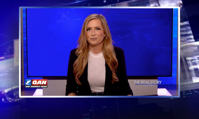 The photo is of Monica Rodriguez at the desk for her talk show. The text on the screen reads "OAN", "THE REAL STORY" and "ONE AMERICA NEWS."