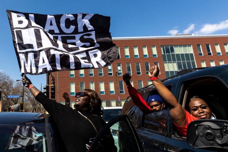 TOPSHOT - A woman holds a Black Lives Matter flag during the funeral service of Daunte Wright outside the Shiloh Temple International Ministries in Minneapolis, April 22, 2021. The Reverend Al Sharpton, the veteran US civil rights leader, is to deliver the eulogy on April 22, 2021 at the funeral of Daunte Wright, a young Black man killed by a policewoman in Minneapolis during the trial of the former police officer convicted of murdering George Floyd.Members of the Floyd family are expected to be among the mourners attending Wright's funeral service at Shiloh Temple International Ministries in Minneapolis. (Photo by Kerem Yucel / AFP) (Photo by KEREM YUCEL/AFP via Getty Images)