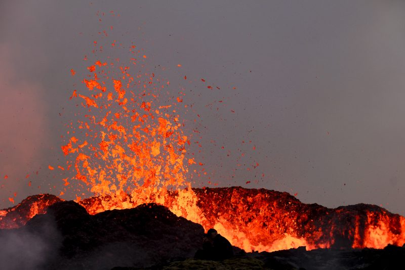 TOPSHOT - People watch flowing lava during an volcanic eruption near Litli Hrutur, south-west of Reykjavik in Iceland on July 10, 2023. A volcanic eruption started on July 10, 2023 around 30 kilometres (19 miles) from Iceland's capital Reykjavik, the country's meteorological office said, marking the third time in two years that lava has gushed out in the area. "The eruption is taking place in a small depression just north of Litli Hrutur, from which smoke is escaping in a north-westerly direction," the office said. Footage circulating in the local media shows a massive cloud of smoke rising from the ground as well as a substantial flow of lava. (Photo by Kristinn Magnusson / AFP) / Iceland OUT (Photo by KRISTINN MAGNUSSON/AFP via Getty Images)