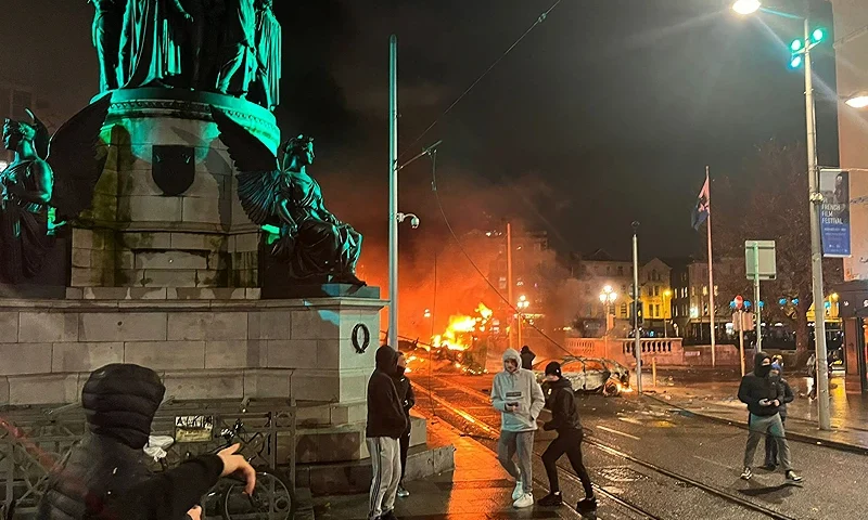 TOPSHOT - Flames rise from a car and a bus, set alight at the junction of Bachelors Walk and the O'Connell Bridge, in Dublin on November 23, 2023, as people took to the streets in protest following the stabbings earlier in the day. Protesters in Dublin on Thursday torched a car and fought police, an AFP journalist reported, after three children were injured in a suspected school stabbing that social media rumours attributed to a foreign national. (Photo by Peter MURPHY / AFP) (Photo by PETER MURPHY/AFP via Getty Images)