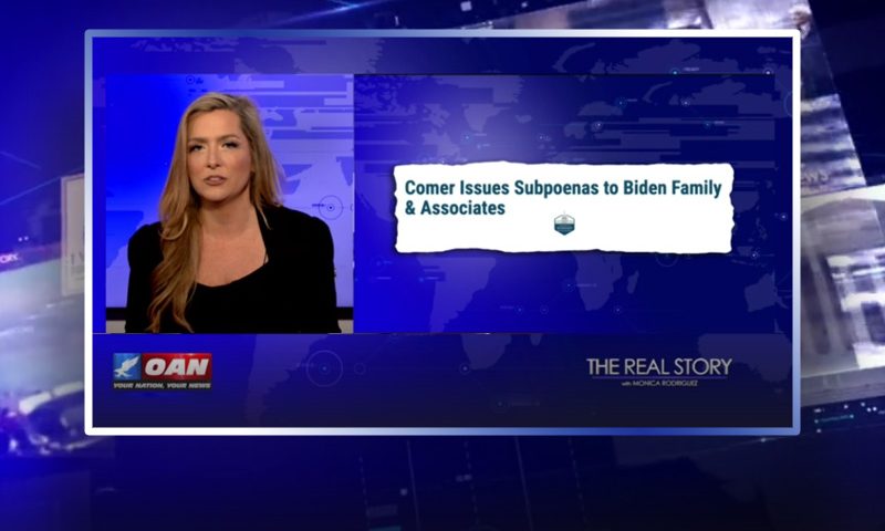Video still of the host of The Real Story at the desk of their talk show on One America News Network.