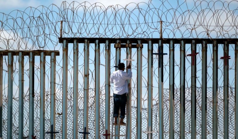 TOPSHOT - Josue Serrano, a Mexican deported migrant, hangs wooden crosses on the border fence as part of a vigil for migrants who died while migrating to the United States, at the US-Mexico border in playas de Tijuana, Baja California state, Mexico, on July 4, 2022. - On June 27, 2022, 53 migrants from Mexico, Guatemala and Honduras were found death abandoned in a suffocatingly hot tractor-trailer truck in the US state of Texas. (Photo by Guillermo Arias / AFP) (Photo by GUILLERMO ARIAS/AFP via Getty Images)