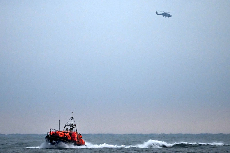 TOPSHOT-BRITAIN-FRANCE-EU-MIGRATION
TOPSHOT - Migrants, picked up at sea attempting to cross the English Channel from France, are brought ashore on a Royal National Lifeboat Institution (RNLI) lifeboat, as a Maritime and Coastguard Agency (MCA) helicopter patrols in the distance, at Dungeness on the southeast coast of England, on December 9, 2022. (Photo by Ben Stansall / AFP) (Photo by BEN STANSALL/AFP via Getty Images)