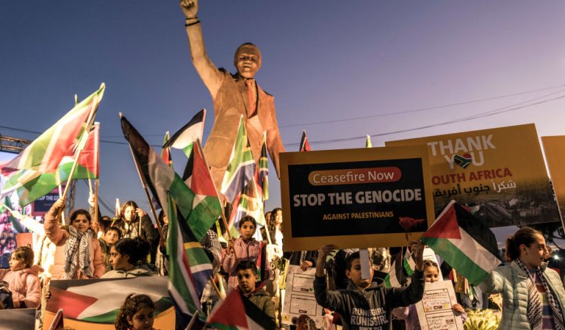 People raise flags and placards as they gather around a statue of late South African president Nelson Mandela to celebrate a landmark "genocide" case filed by South Africa against Israel at the International Court of Justice, in the occupied West Bank city of Ramallah on January 10, 2024. The ruling African National Congress (ANC) has long been a firm supporter of the Palestinian cause, often linking it to its own struggle against the white-minority government, which had cooperative relations with Israel. (Photo by MARCO LONGARI / AFP) (Photo by MARCO LONGARI/AFP via Getty Images)