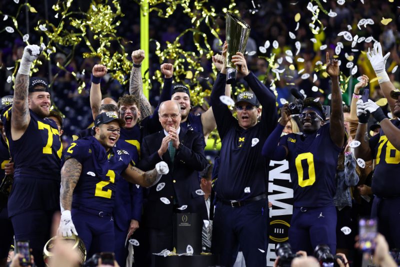 HOUSTON, TEXAS - JANUARY 08: Head coach Jim Harbaugh of the Michigan Wolverines and his team react as he lifts the national championship trophy after defeating the Washington Huskies during the 2024 CFP National Championship game at NRG Stadium on January 08, 2024 in Houston, Texas. Michigan defeated Washington 34-13. (Photo by Maddie Meyer/Getty Images)