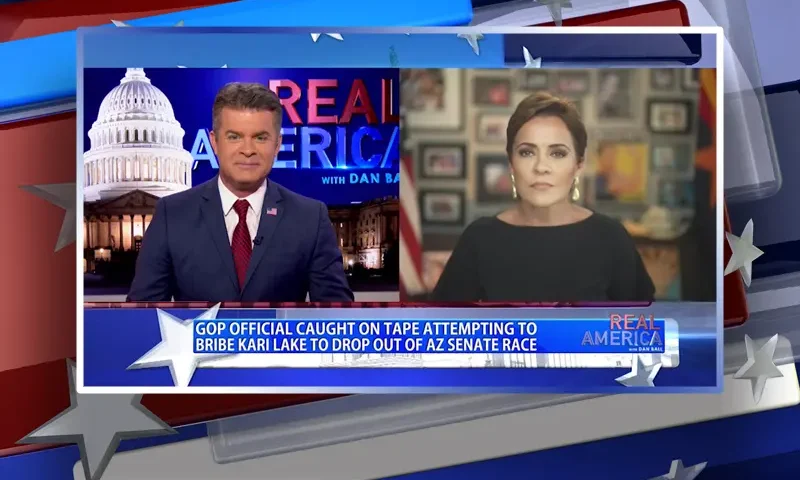 Video still from Real America on One America News Network showing a split screen of the host on the left side, and on the right side is the guest, Kari Lake.