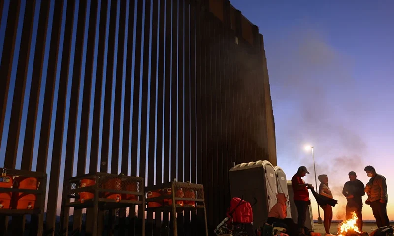 YUMA, ARIZONA - MAY 22: Immigrants from Cuba and Venezuela warm themselves by a fire before sunrise along the U.S.-Mexico border barrier as they await processing by the U.S. Border Patrol after crossing from Mexico on May 22, 2022 in Yuma, Arizona. Title 42, the controversial pandemic-era border policy enacted by former President Trump, which cites COVID-19 as the reason to rapidly expel asylum seekers at the U.S. border, was set to officially expire on May 23rd. A federal judge in Louisiana delivered a ruling May 20th blocking the Biden administration from lifting Title 42. (Photo by Mario Tama/Getty Images)
