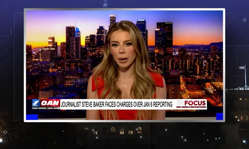 Video still of the host of In Focus at the desk of their talk show on One America News Network.