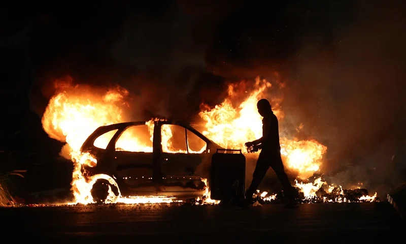 TOPSHOT-FRANCE-OVERSEAS-CRIME-POLICE-DEMO TOPSHOT - A protester walks by a burning car during clashes with police in Le Port, French Indian Ocean island of La Reunion, on June 30, 2023, three days after a 17-year-old boy was shot in the chest by police at point-blank range in Nanterre, a western suburb of Paris. A third consecutive night of violence in France sparked by the killing of a teenager by a policeman during a traffic stop has left 249 police and gendarmes injured, the interior ministry announced on June 30, 2023. (Photo by Richard BOUHET / AFP) (Photo by RICHARD BOUHET/AFP via Getty Images)