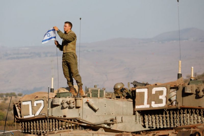 TOPSHOT - An Israeli soldier places a national flag atop a Merkava tank during in a military drill near the border with Lebanon in the upper Galilee region of northern Israel on October 26, 2023, amid the ongoing battles between Israel and the Palestinian group Hamas in the Gaza Strip. (Photo by Jalaa MAREY / AFP) (Photo by JALAA MAREY/AFP via Getty Images)