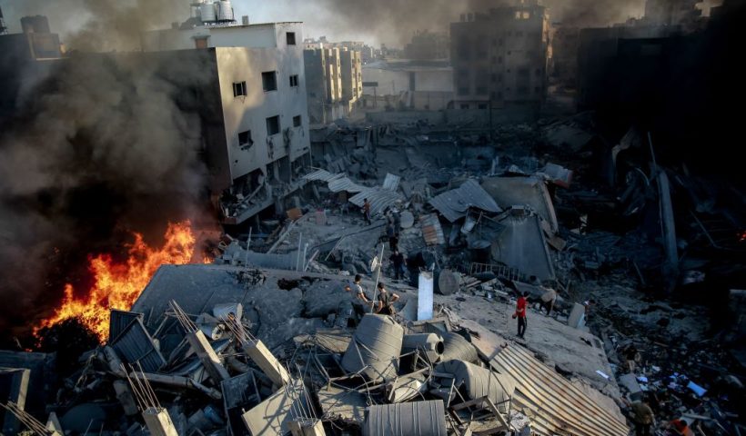 TOPSHOT - Smoke and fire rise from a levelled building as people gather amid the destruction in the aftermath of an Israeli strike on Gaza City on October 26, 2023, as battles continue between Israel and the Palestinian Hamas group. (Photo by Omar El-Qattaa / AFP) (Photo by OMAR EL-QATTAA/AFP via Getty Images)