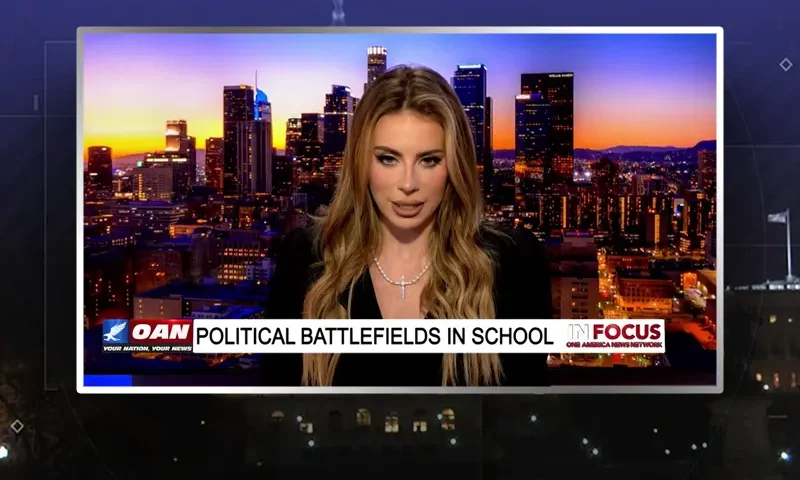 Video still of the host of In Focus at the desk of their talk show on One America News Network.