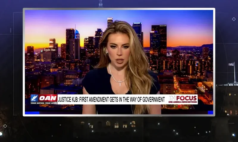 Video still of the host of In Focus at the desk of their talk show on One America News Network.