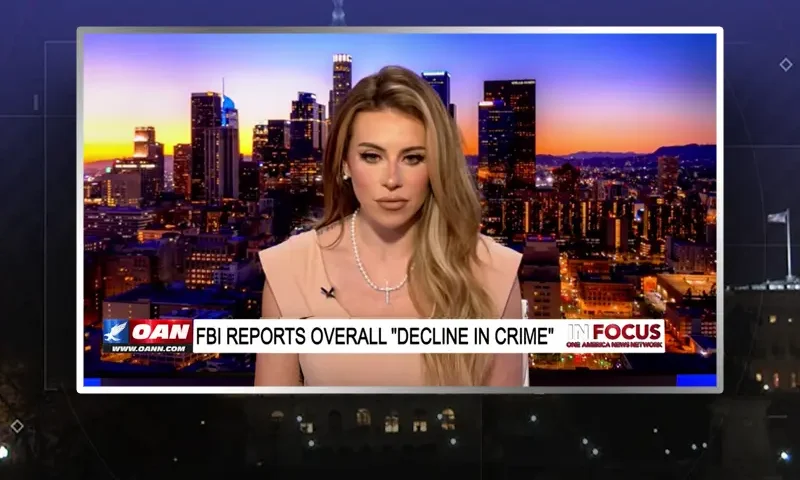 Video still of the host of In Focus at the desk of their talk show on One America News Network.