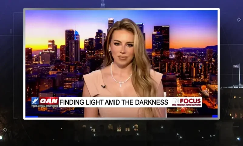 Video still of the host of In Focus at the desk of their talk show on One America News Network.