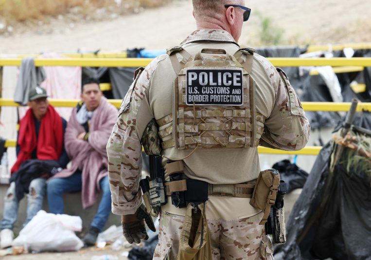 SAN DIEGO, CALIFORNIA - MAY 13: A Customs and Border Protection officer keeps watch as immigrants are transported from a makeshift camp between border walls between the U.S. and Mexico on May 13, 2023 in San Diego, California. Some of the immigrants at the open air camp have been waiting for days in limbo for a chance to plead for asylum while local volunteer groups are providing food and other necessities. The U.S. government's Covid-era Title 42 policy, which for the past three years had allowed for the quick expulsion of irregular migrants entering the country, expired on the evening of May 11. (Photo by Mario Tama/Getty Images)