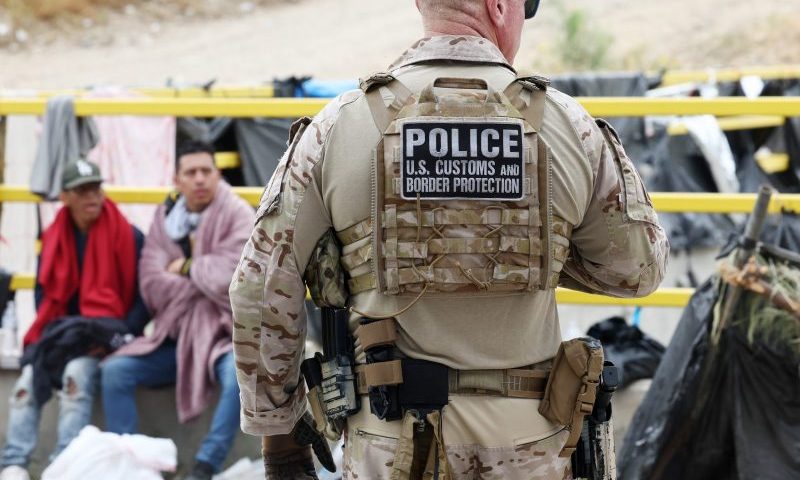 SAN DIEGO, CALIFORNIA - MAY 13: A Customs and Border Protection officer keeps watch as immigrants are transported from a makeshift camp between border walls between the U.S. and Mexico on May 13, 2023 in San Diego, California. Some of the immigrants at the open air camp have been waiting for days in limbo for a chance to plead for asylum while local volunteer groups are providing food and other necessities. The U.S. government's Covid-era Title 42 policy, which for the past three years had allowed for the quick expulsion of irregular migrants entering the country, expired on the evening of May 11. (Photo by Mario Tama/Getty Images)