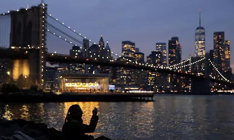 A person takes a photo while looking toward the Manhattan skyline on the Winter Solstice in Brooklyn, New York City, U.S., December 21, 2021. REUTERS/Andrew Kelly/File Photo