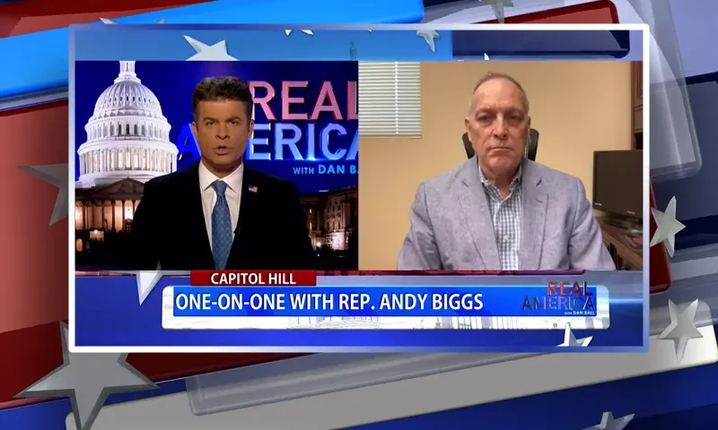Video still from Real America on One America News Network showing a split screen of the host on the left side, and on the right side is the guest, Rep. Andy Biggs.