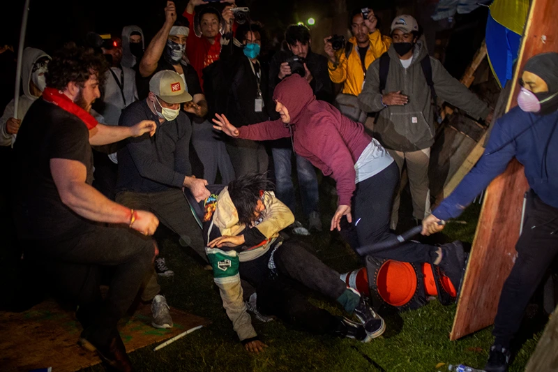 Demonstrators clash at an encampment at UCLA early Wednesday, May 1, 2024, in Los Angeles.  Dueling groups of protesters have clashed at the University of California, Los Angeles, grappling in fistfights and shoving, kicking and using sticks to beat one another. (AP Photo/Ethan Swope)