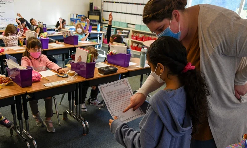 CENTREVILLE, VA - OCTOBER 19: Kaitlin North, 2nd grade teacher at Colin L. Powell Elementary School, helps a student read aloud a letter they wrote to the family of Colin Powell with their condolences after news of his passing due to COVID-19 complications was announced, on October 19, 2021 in Centreville, Virginia. Students and faculty at the school, which is named after the former Secretary of State, honored his legacy by lowering the school's flag to half-staff, watching a video of Powell and holding a moment of silence. (Photo by Kenny Holston/Getty Images)