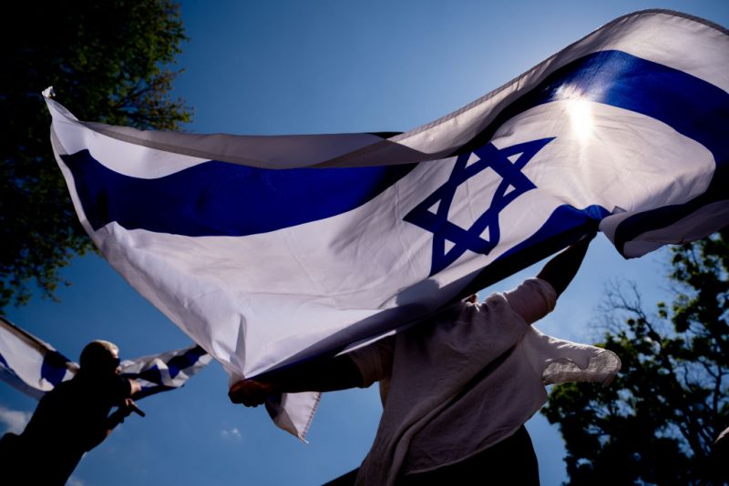 WASHINGTON, DC - MAY 2: Michal Rokah of Falls Church, Virginia (C) and Israeli Matan Showstack of Washington, DC (L) dance and wave large Israeli flags during a rally against campus antisemitism at George Washington University on May 2, 2024 in Washington, DC. A pro-Palestinian rally was also held at the school today, as protestors at college campuses around the country call for schools to divest from Israeli interests amid the ongoing war in Gaza. (Photo by Andrew Harnik/Getty Images)