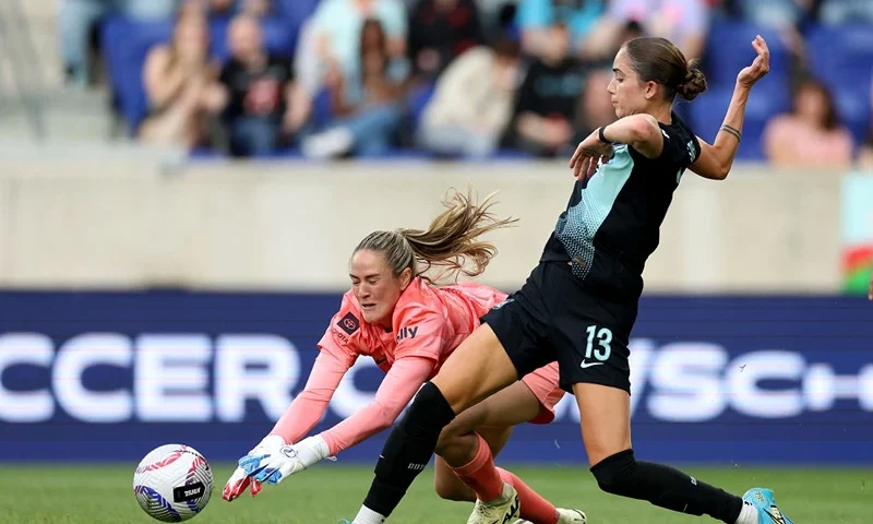 HARRISON, NEW JERSEY - APRIL 28: Katie Lund #1 of Racing FC falls as Ella Stevens #13 passes and gets the assist on a goal scored by teammate Rose Lavelle during the second half at Red Bull Arena on April 28, 2024 in Harrison, New Jersey. The Racing Louisville FC and the NJ/NY Gotham FC tied at 1-1. (Photo by Elsa/Getty Images)