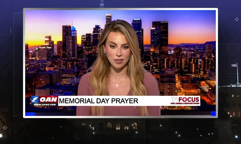 Video still of the host of In Focus at the desk of their talk show on One America News Network.
