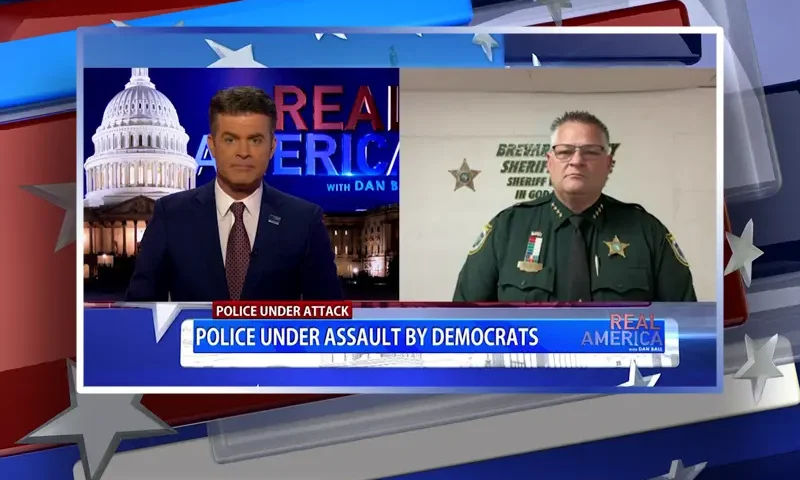 Video still from Real America on One America News Network showing a split screen of the host on the left side, and on the right side is the guest, Sheriff Wayne Ivey.