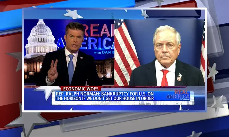 Video still from Real America on One America News Network showing a split screen of the host on the left side, and on the right side is the guest, Ralph Norman.