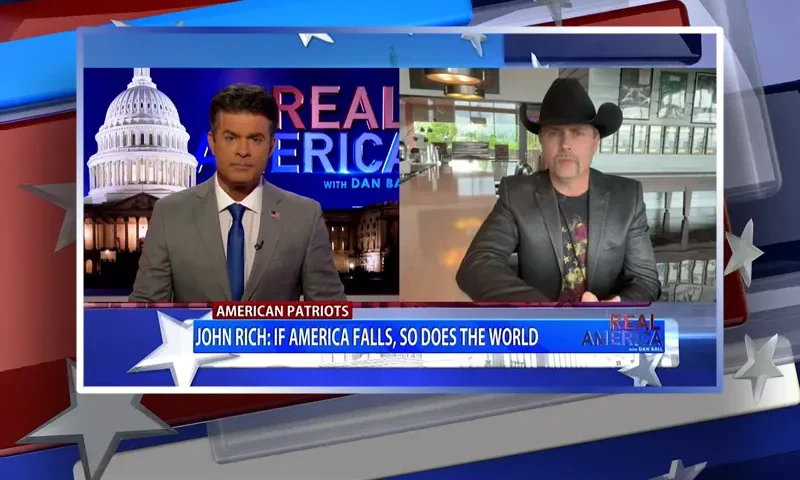 Video still from Real America on One America News Network showing a split screen of the host on the left side, and on the right side is the guest, John Rich.