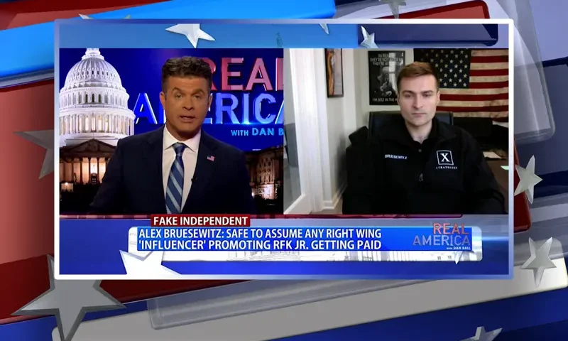 Video still from Real America on One America News Network showing a split screen of the host on the left side, and on the right side is the guest, Alex Bruesewitz.