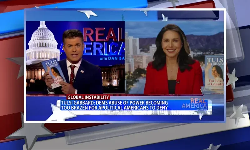 Video still from Real America on One America News Network showing a split screen of the host on the left side, and on the right side is the guest, Tulsi Gabbard.